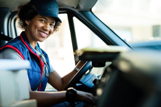 A smiling woman sits in the driver’s seat of a delivery van.