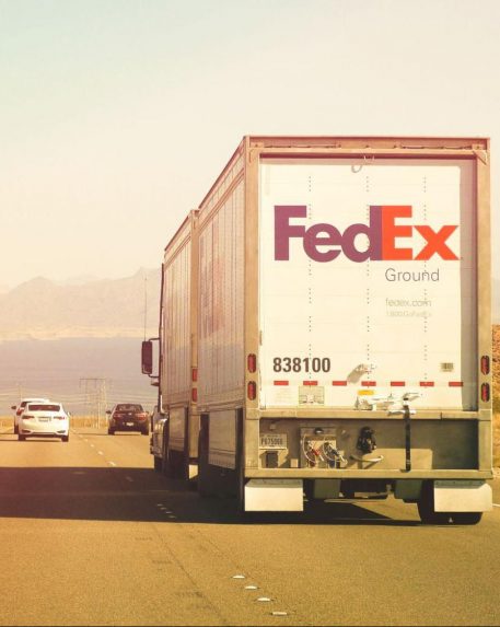 A white FedEx truck drives down a highway through the desert.